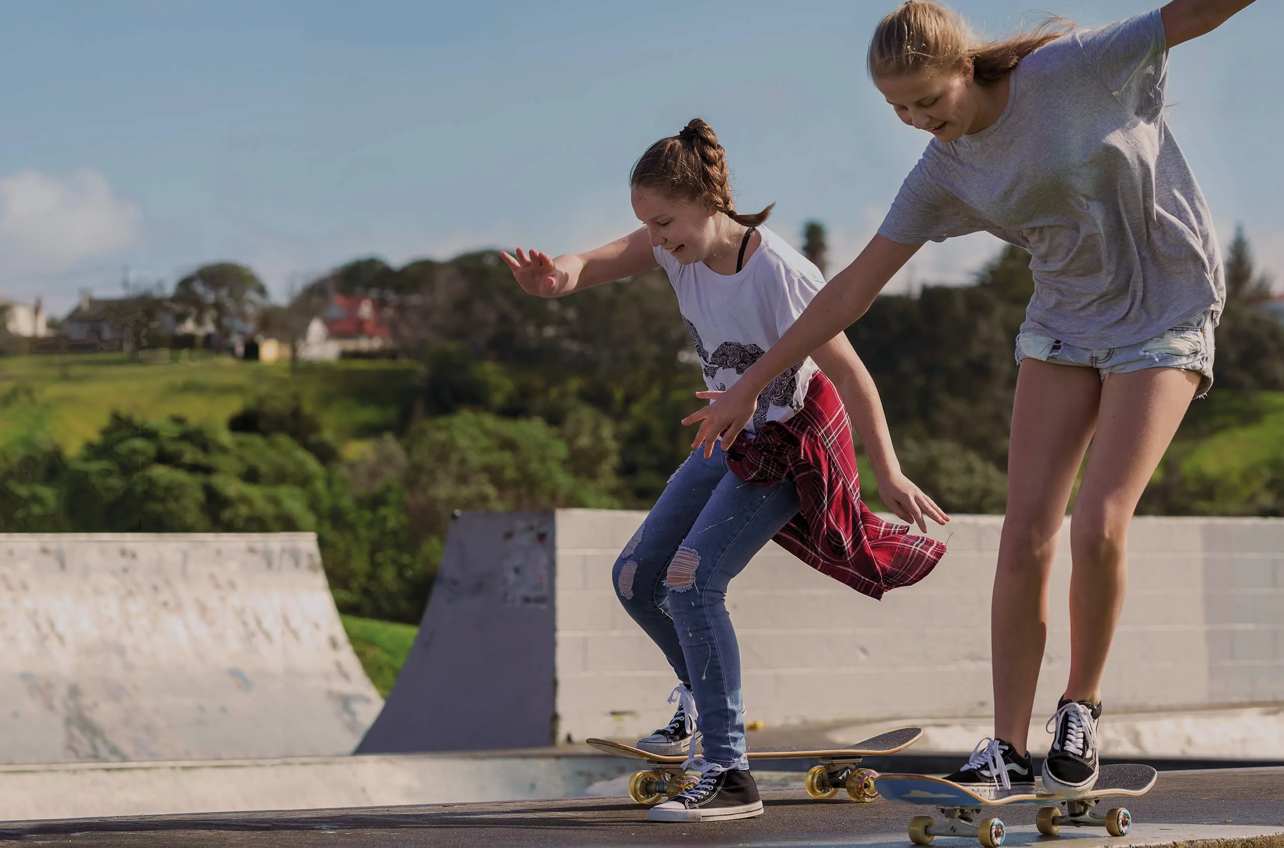 Two Girls Riding Skateboards At Skatepark